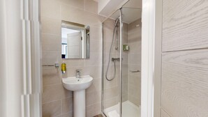 Un baño moderno con cabina de ducha de vidrio, un lavamanos blanco pedestal y un espejo sobre el lavamanos.
