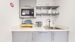 Cocina moderna con microondas, hervidor, pileta y estanterías.