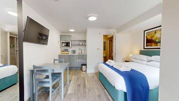 A hotel room with a bed, a desk with chairs, a kitchenette, and a shower area.