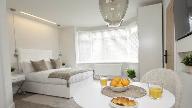A modern bedroom with a bed, bedside table, and a breakfast setup on a small table with a bowl of fruit and juice glasses. - Bell House Oxford - The Quill (Oxford)