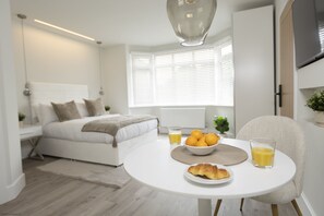 Een moderne slaapkamer met een bed, nachtkastje en een ontbijtje op een tafeltje, met een schaal fruit en sapglazen.
