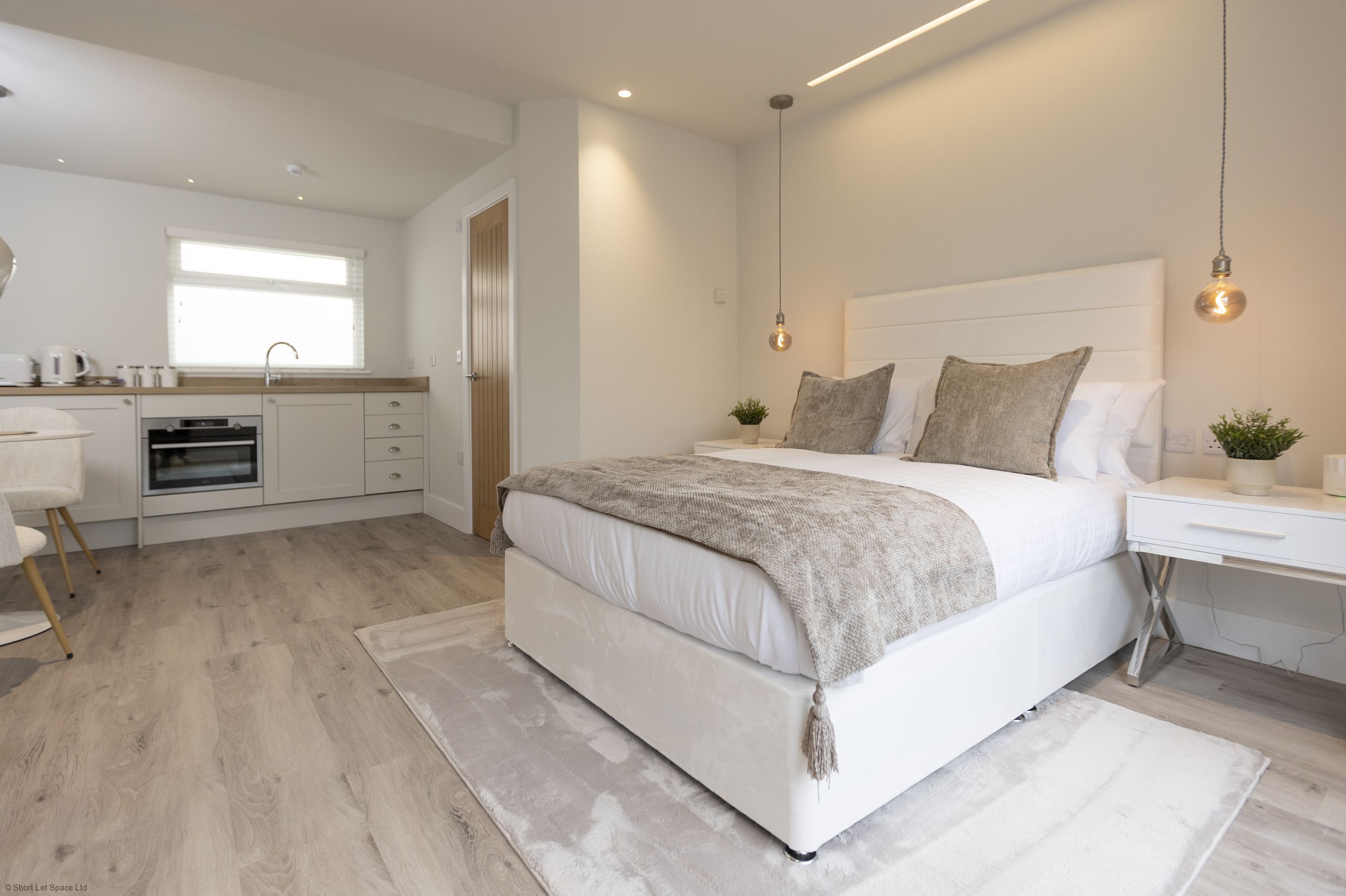 Un dormitorio moderno con una cama grande, mesitas de noche, un escritorio y una zona de cocina.