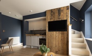 Cocina moderna con armarios blancos, una pared de acento de madera y un televisor de pantalla plana montado sobre la encimera.