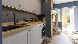 A modern kitchen with a wooden countertop, stainless steel sink, and built-in oven. - Bell House Oxford - The Noke (Oxford)