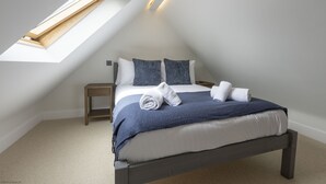 A bedroom with a sloped ceiling, a skylight, a bed with a blue blanket, two pillows, and two rolled towels on the bed. - Bell House Oxford - The Noke (Oxford)