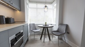A modern kitchen with grey cabinetry, a built-in oven, a round dining table with two chairs, and a hanging pendant light. - Bell House Oxford - The Punt (Oxford)