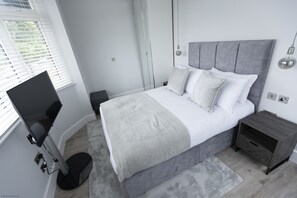Et moderne soveværelse med en stor seng, sengeborde, et skrivebord og en gulvlampe.