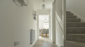 A hallway with a carpeted staircase, a radiator, and a dining area in the background. - Wren House in Bicester (Bicester)
