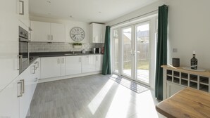 A modern kitchen with white cabinets, a black countertop, and a wooden bench. - Wren House in Bicester (Bicester)