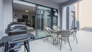 Un patio con puerta de vidrio que da a una cocina, sillas de mimbre y una parrilla.