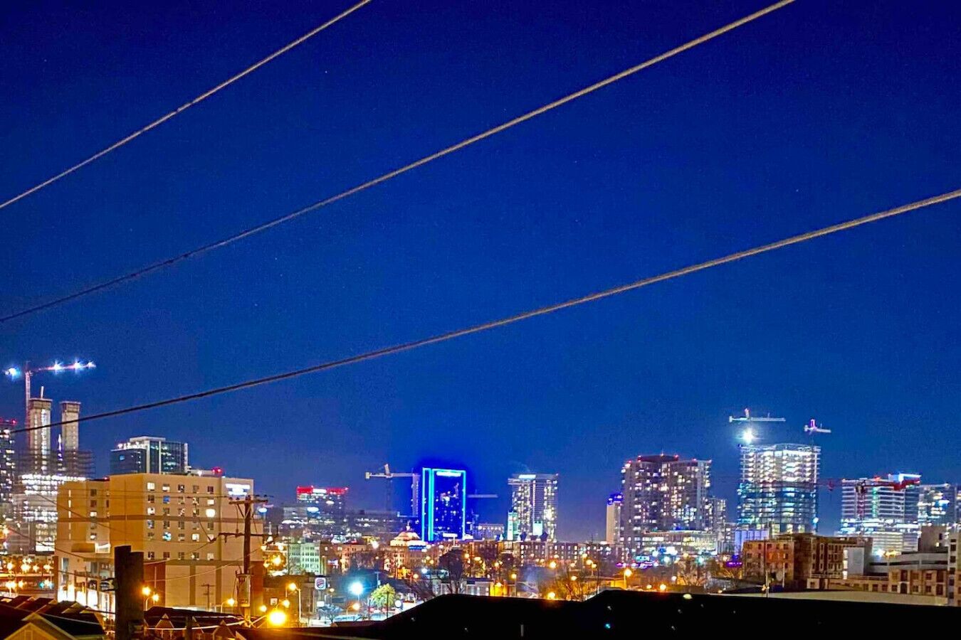 Een verlicht stadsbeeld bij nacht, met gebouwen en elektriciteitskabels.