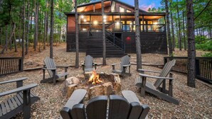 A cabin with a fire pit and Adirondack chairs in a forest setting. - Timberline Pines · Spacious Escape | Hot Tub, Fireplaces & Soaking Tub (Broken Bow)