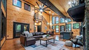 A spacious living area with a leather sofa, a coffee table, and a staircase leading to an upper level. - Timberline Pines · Spacious Escape | Hot Tub, Fireplaces & Soaking Tub (Broken Bow)