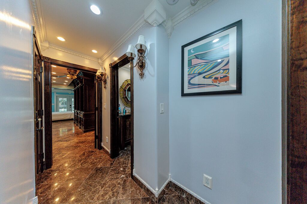 A hallway with marble flooring, a framed abstract painting, and a wall-mounted light fixture.