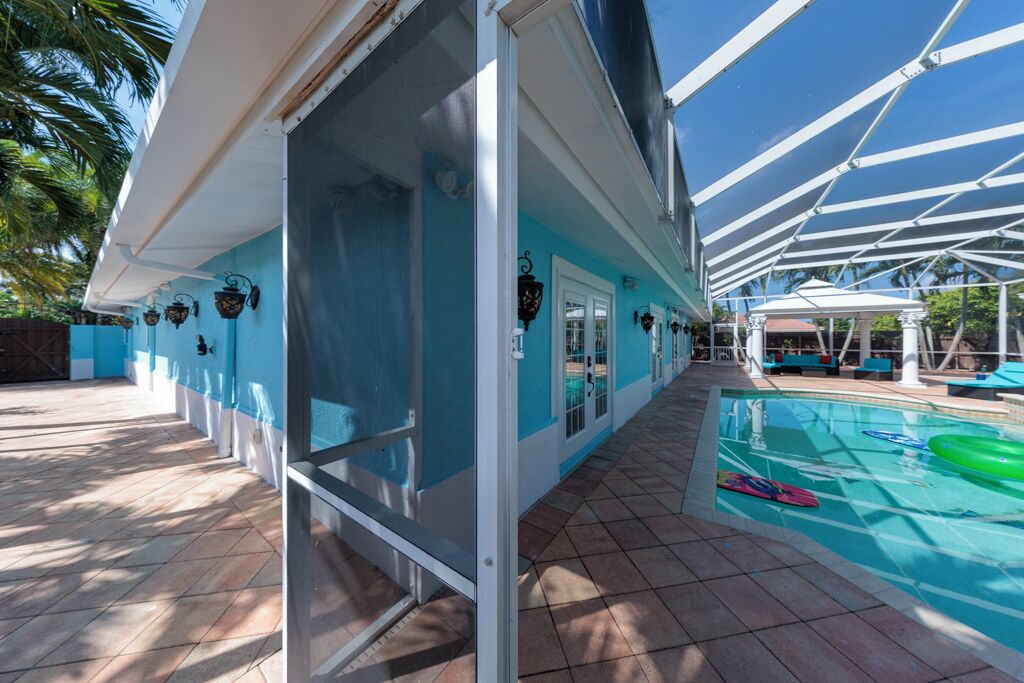 A pool area with a covered deck, a clear blue sky, and a tiled floor.