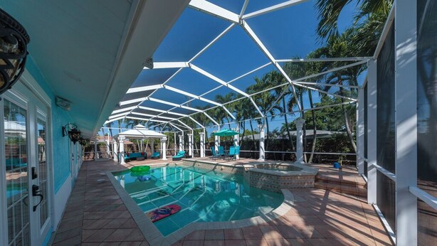 A covered pool area with a clear blue sky, palm trees, and a tiled floor.