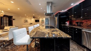 A modern kitchen with a marble countertop, stainless steel appliances, and white bar stools.