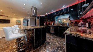 A modern kitchen with black cabinets, a marble countertop, and a stainless steel range hood.