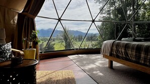 A bedroom with a large window offering a view of mountains and greenery. - Hanmer Glamping (Hanmer Springs)