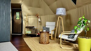 A tented room with a wooden floor, a small round table, a chair with a cushion, a lamp, and a potted plant. - Hanmer Glamping (Hanmer Springs)