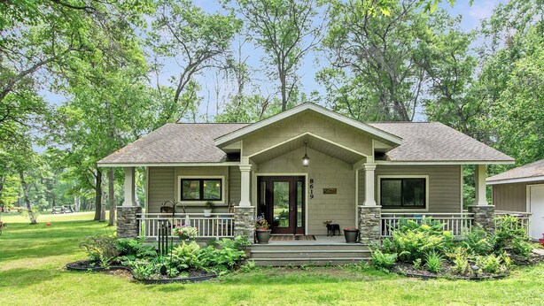 A two-story house with a front porch, stone pillars, and a well-maintained lawn. - NEW! All Season Hot Tub, Fire Pit, Golf Course, Breezy Point (Pequot Lakes)