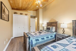 A bedroom with a wooden ceiling, a bed with a quilted blanket, a nightstand with a lamp, and a door leading to another room. - NEW! All Season Hot Tub, Fire Pit, Golf Course, Breezy Point (Pequot Lakes)