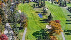 A golf course with a pond, surrounded by trees with autumn foliage, and a view of a body of water. - NEW! All Season Hot Tub, Fire Pit, Golf Course, Breezy Point (Pequot Lakes)