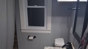 Une salle de bain avec des toilettes blanches, un lavabo doté d’un plan de toilette en marbre et une fenêtre située au-dessus des toilettes.