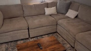 Un salon avec un canapé d’angle, une table basse en bois et un tapis à motifs.