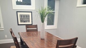 Une table à manger entourée de six chaises en bois, un vase avec une plante et des tableaux encadrés accrochés au mur.