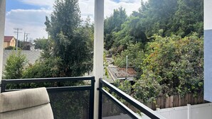 A balcony with a view of a densely wooded area and a distant building.