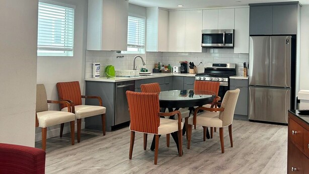 A modern kitchen with white cabinets, stainless steel appliances, and a dining area with wooden chairs.