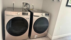 A laundry room with two front-loading washing machines, a power outlet, and a wall-mounted electrical outlet.