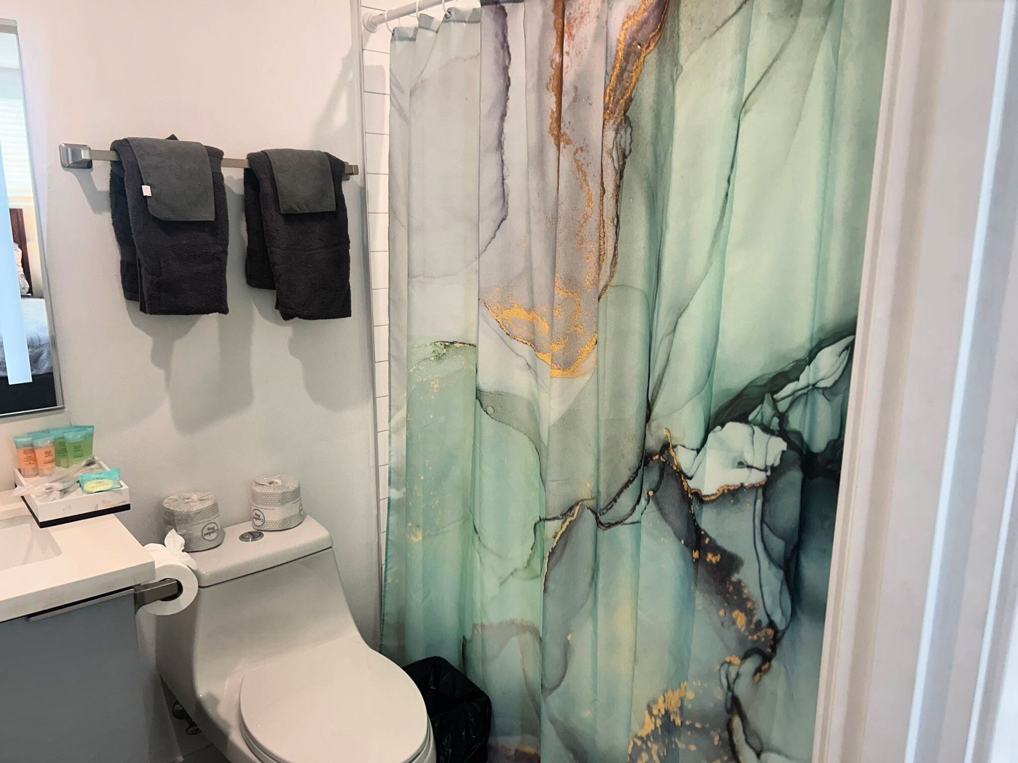 A bathroom with a toilet, a shower curtain with a leaf pattern, and a towel rack with three towels.