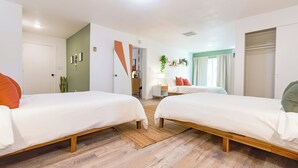 A modern hotel room with two single beds, a wooden floor, a small desk, and a view of the city. - Cozy Cactus - Cowboy Pool, Outdoor Movies, 3BR - Walk to Saloon (Joshua Tree)
