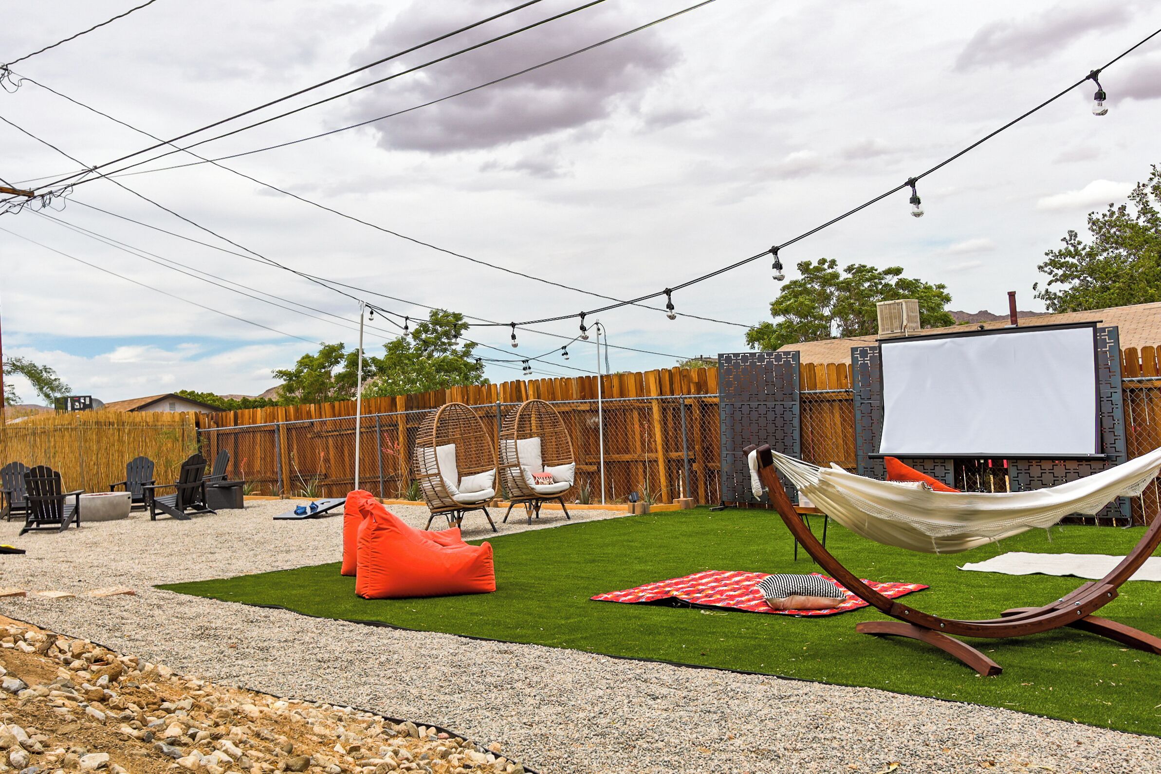 A backyard with artificial grass, a hammock, outdoor seating, and a white screen.