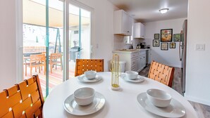 A modern kitchen with white cabinets, a dining table set with white plates and bowls, and a view of the outdoor patio area. - Cozy Cactus - Cowboy Pool, Outdoor Movies, 3BR - Walk to Saloon (Joshua Tree)