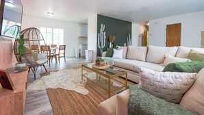 A modern living room with a glass coffee table, a sofa, and a dining area with chairs and a table. - Cozy Cactus - Cowboy Pool, Outdoor Movies, 3BR - Walk to Saloon (Joshua Tree)
