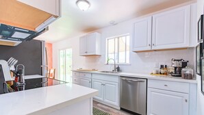 A modern kitchen with white cabinets, stainless steel appliances, and a window providing natural light. - Cozy Cactus - Cowboy Pool, Outdoor Movies, 3BR - Walk to Saloon (Joshua Tree)