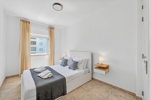 Une chambre d’hôtel moderne avec un grand lit, deux lampes de chevet, une table de chevet en bois et une vue sur un bâtiment à l’extérieur.
