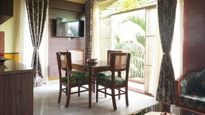 Comedor con mesa y sillas, televisor montado en la pared y vista al exterior a través de un ventanal grande.