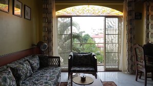 Una habitación con sofá, una silla, una mesa y un amplio ventanal con vistas a zonas verdes y edificios.