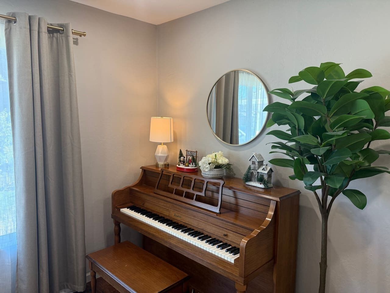 Een piano met een bankje, een lamp, een spiegel en een potplant in een kamer met lichte muren.