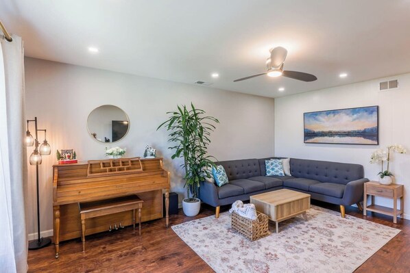 A living room with a piano, a sofa, a coffee table, a plant, and a painting on the wall.