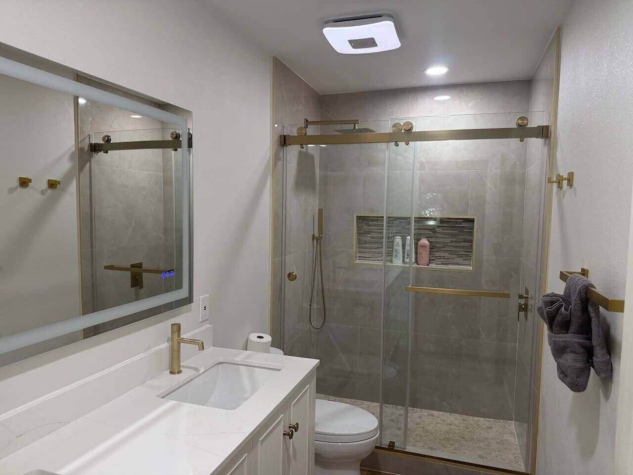 A bathroom with a glass-enclosed shower, a white sink with gold fixtures, a toilet, and a mirror.