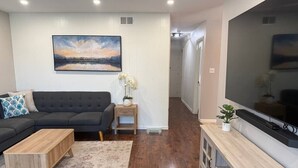 Ein Wohnzimmer mit einem dunklen Sofa, einem Holztisch, einem Fernseher auf einem Holzständer und einem Gemälde an der Wand.