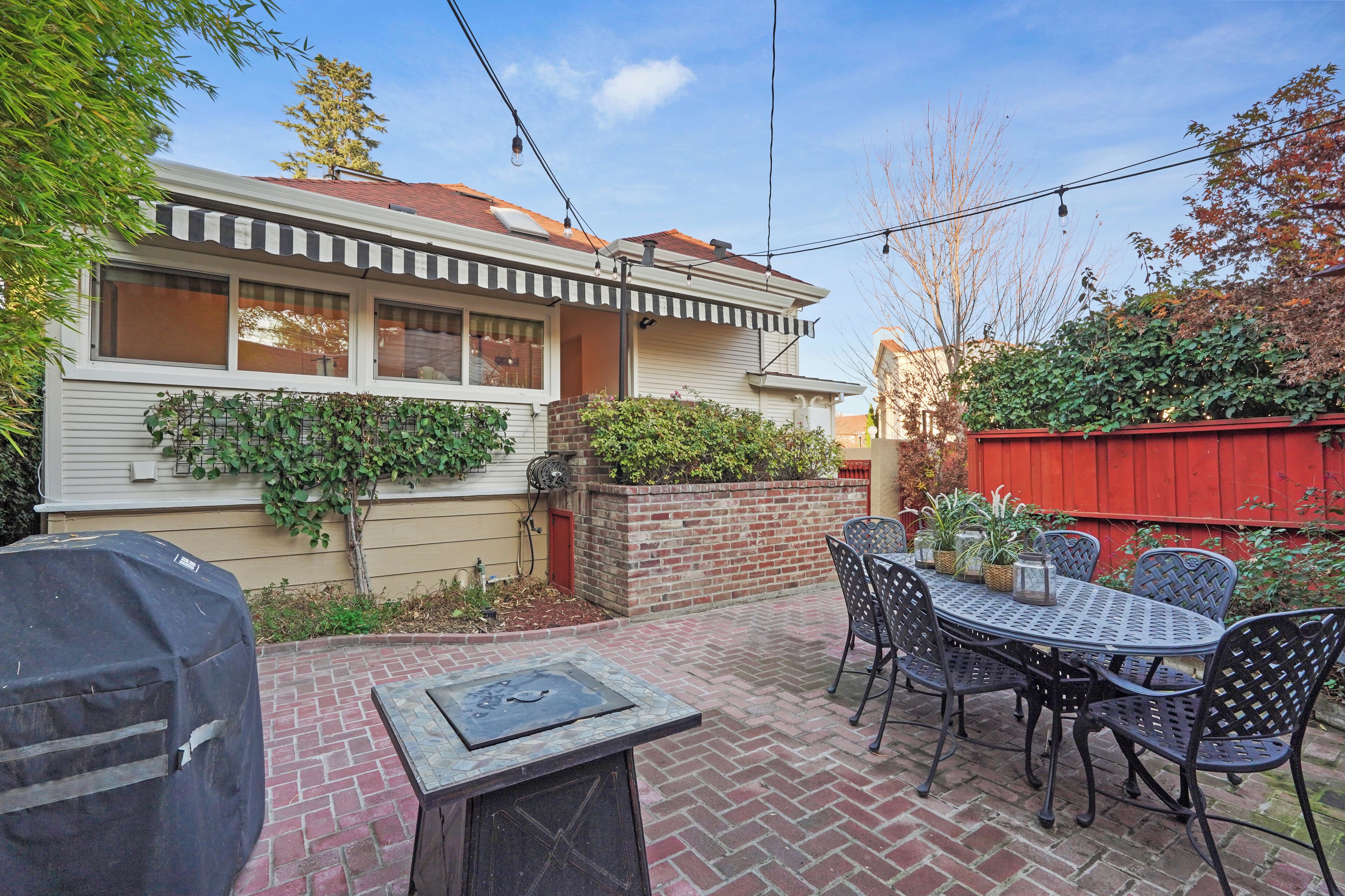 A patio area with a brick floor, a round metal table, and black metal chairs.