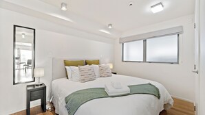 Um quarto com uma cama, mesa de cabeceira, espelho e janela.