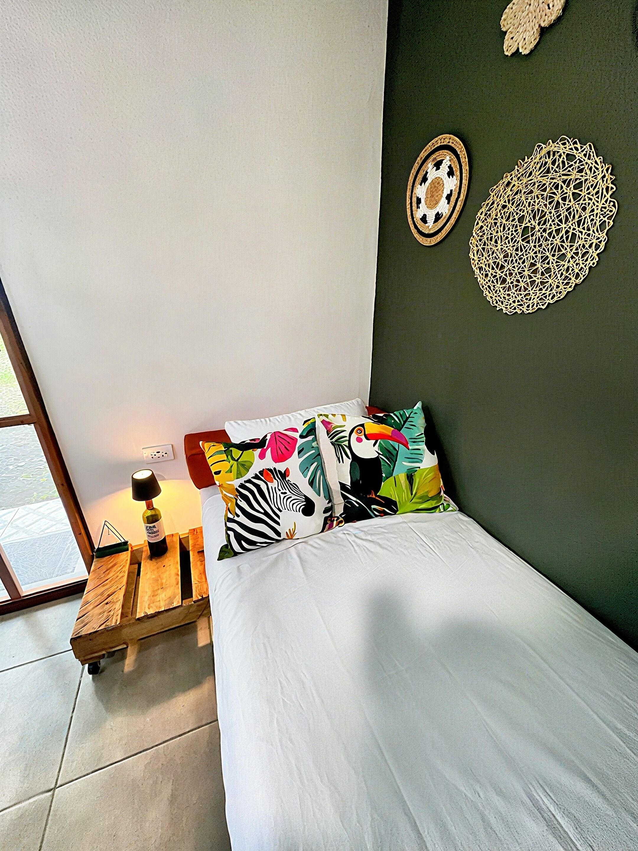 A bedroom with a bed, a nightstand with a lamp, and a window.
