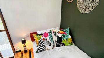 A bedroom with a bed, a nightstand with a lamp, and a window.